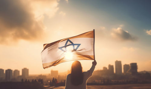 Low angle view of woman holding flag against sky during sunset