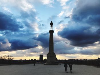 People at historical building in city against cloudy sky