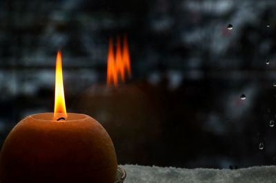 Close-up of burning candle by window