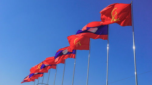 Low angle view of flags waving against clear blue sky