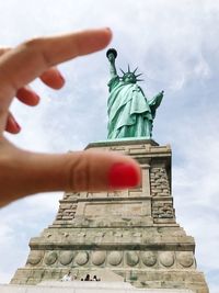 Optical illusion of hand gesturing tiny sign against statue of liberty