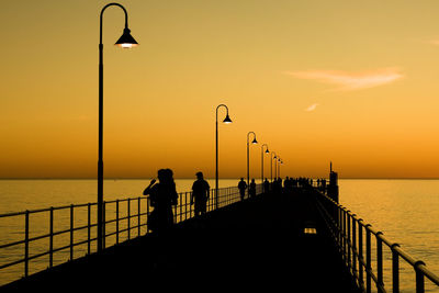 Silhouette people on a jetty by sea against sky during sunset