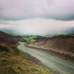 Empty road by countryside landscape against cloudy sky