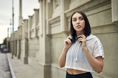 Thoughtful jogger with headphones looking away while standing on sidewalk