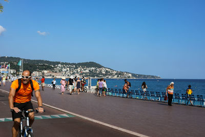 People riding bicycle on sea by city against sky