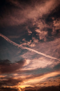 Low angle view of vapor trails in sky during sunset