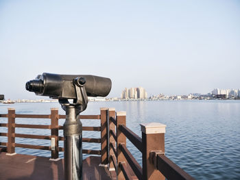 Coin-operated binoculars on wooden post by sea against clear sky
