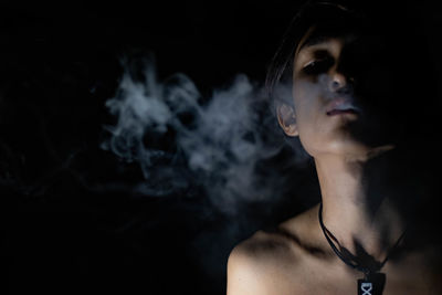 Portrait of man smoking against black background