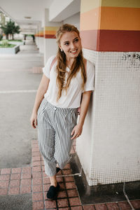 Full length of smiling young woman standing by column