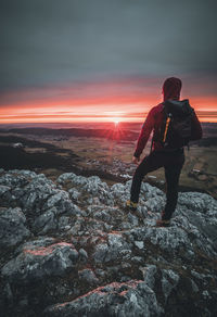 Man standing on rock against sky during sunset