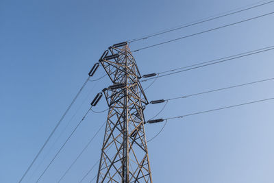 Low angle view of electricity pylon against clear blue sky