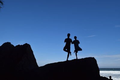Silhouette people on rock against blue sky