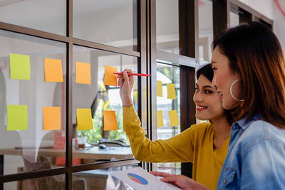 Colleagues writing on adhesive notes while standing in office