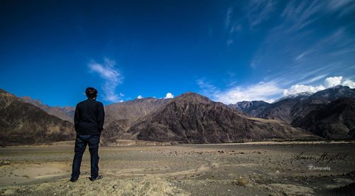 Rear view of man standing on landscape against blue sky