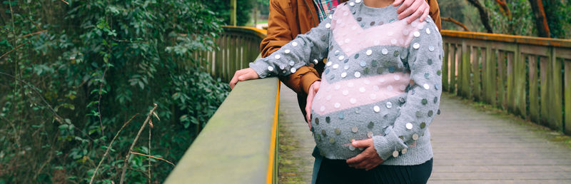 Pregnant woman holding her belly next to man over pathway on nature