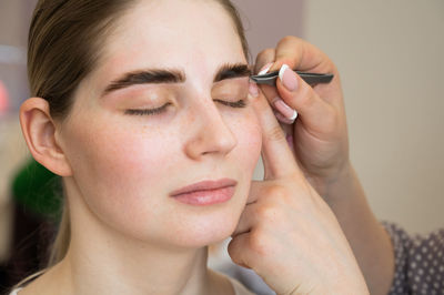 Close-up portrait of young woman applying make-up