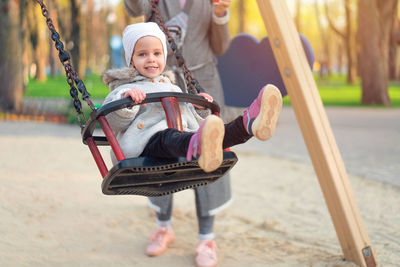 Portrait of cute girl wearing warm clothing while swinging at playground