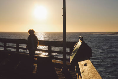 Woman standing on pier by sea against clear sky