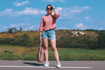 Portrait of young woman wearing sunglasses standing on road