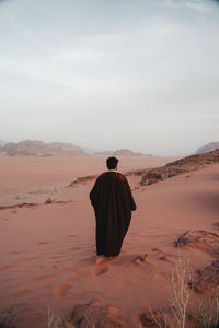 Rear view of man walking at desert against sky