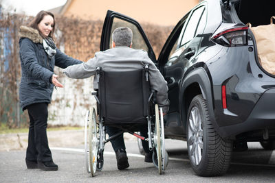A woman helps aphysical disabled person to get into the car.