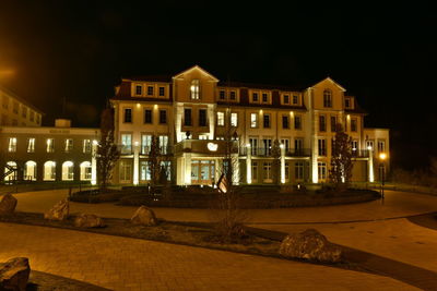 Illuminated buildings by street against sky at night