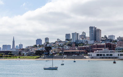 Sailboats in city by buildings against sky