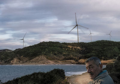 Portrait of man against wind turbines on mountain and lake