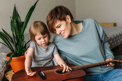 Little girl plays the guitar with her mother on the floor at home