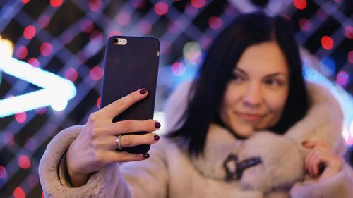 Young woman photographing with mobile phone at night