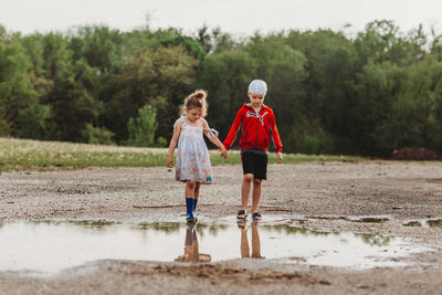 Siblings walking in puddle at beach against sky