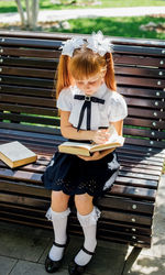 A child is sitting on a bench outside on a warm sunny day, and is returning to school. 