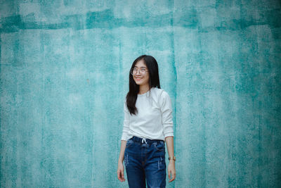 Portrait of a smiling young woman standing against wall