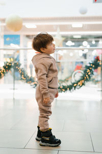 Four year old boy in a warm tracksuit stands in a shopping center and looks intently