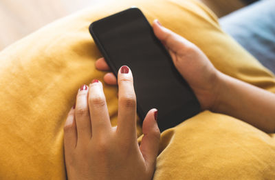 Cropped hands of woman using phone on cushion at home
