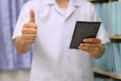 Midsection of man showing thumbs up while holding digital tablet