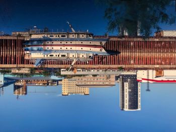 Sailboats in river by buildings against blue sky