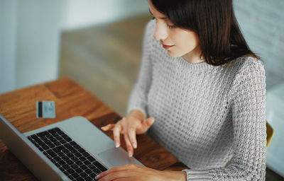 Woman using laptop by credit card for online shopping on table