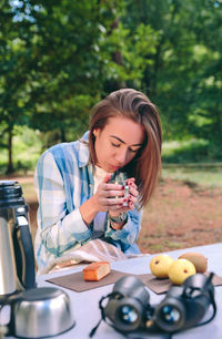 Woman holding tea cup while sitting on chair at forest