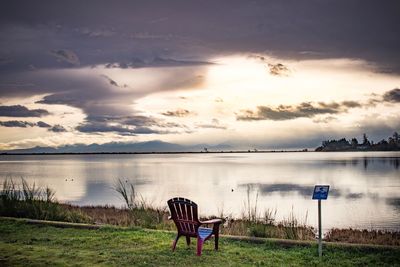 Chairs on grass by lake against sky