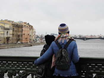 Rear view of mother and daughter looking at river in city during winter