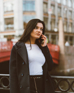 Young woman talking on mobile phone while standing in city