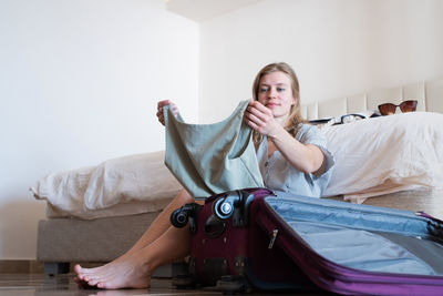 Portrait of woman sitting on bed at home packing bags 