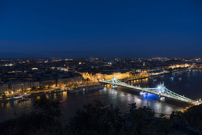 Illuminated bridge over river in city against sky at night