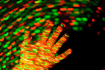 Cropped hand of person with multi colored lights against black background