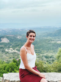 Portrait of smiling woman standing on rock against mountain