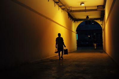 Silhouette man walking in illuminated tunnel at night