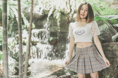 Portrait of beautiful young woman standing against trees