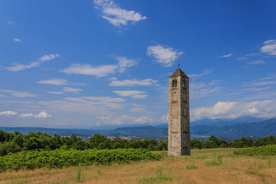 Tower on field by building against sky