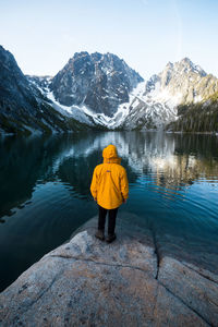 Rear view of person standing by lake against mountains and sky